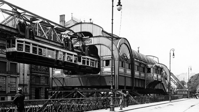 Historischer Bahnhof mit historischer Architektur und einem abgestellten Personenzug auf erhöhten Gleisen.