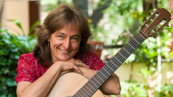 Eine Frau lehnt sich auf ihre Gitarre vor einem Hintergrund voller Pflanzen