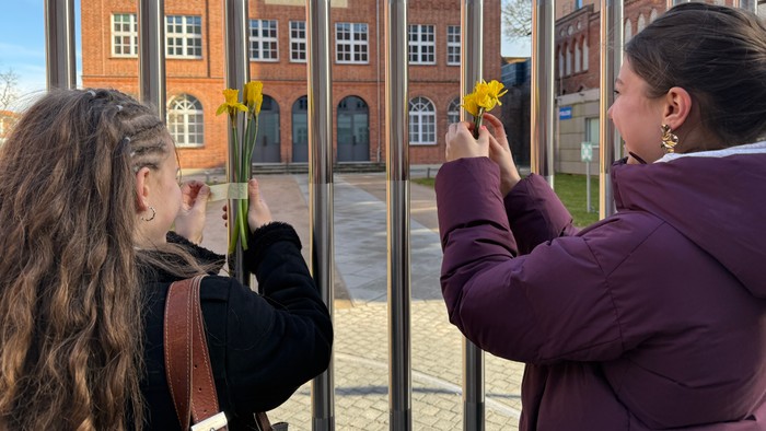 Zwei Mädchen bringen Narzissen am Zaun vor der Synagoge als Zeichen des Gedenkens an.