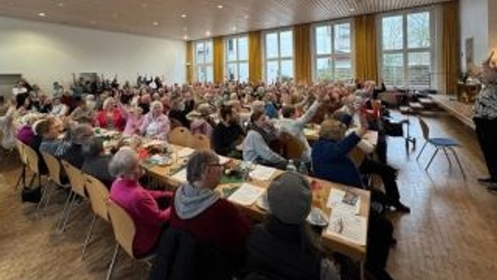 Eine große Gruppe von Menschen versammelt sich in einem Hörsaal, an Tischen sitzend mit Papieren und Laptops.