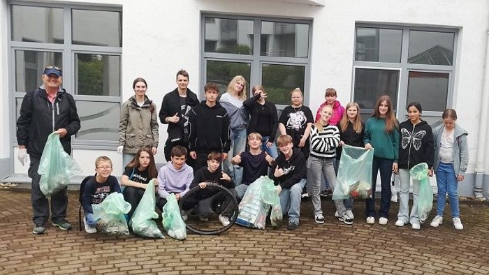 Gruppe von Menschen, die Müllsäcke halten und nach einer Aufräumaktion gemeinsam vor einem Gebäude posieren.