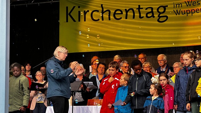 Ein Chor tritt bei einer Open-Air-Veranstaltung des Kirchentags mit Konfetti und Publikum auf der Bühne auf.