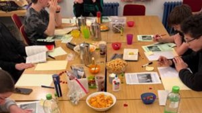 Gruppe, die an einem Tisch mit Snacks, Getränken und verschiedenen Kunstmaterialien während eines Workshops zusammenarbeitet.