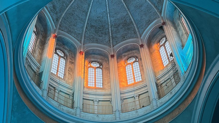Das Bild zeigt eine Kuppelhalle mit großen Fenstern und blauen Wänden.