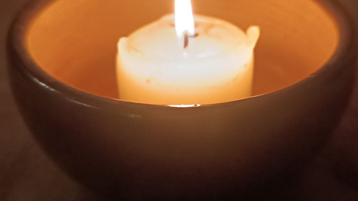 Eine brennende Kerze in einer dunklen, warmtönigen Schale, die sanftes, mildes Licht wirft.