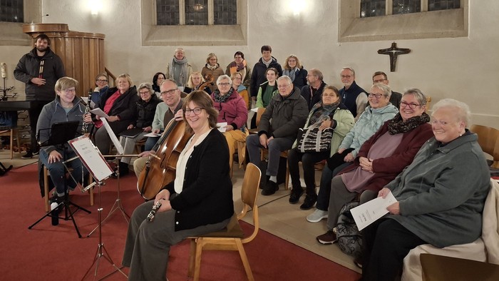 Eine Gruppe versammelt sich in einer Kirche zu einer musikalischen Darbietung, wobei ein Cellist im Vordergrund deutlich platziert ist.