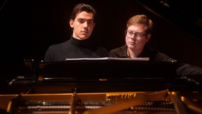 To musikere spiller sammen på et flygel, dybt koncentreret om deres optræden.