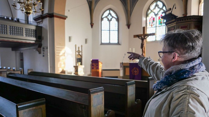 Eine Frau zeigt aus dem Seitengang einer Kirche auf den Altarraum