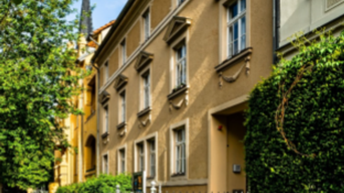 Ein beigefarbenes Wohngebäude mit Fahrrädern davor und üppigem Grün.