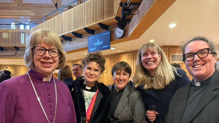 A group of women in formal attire posing together, including clergy in purple and black robes.