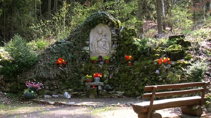 Ein friedvoller Waldschrein, geschmückt mit Blumen und moosbewachsenen Steinskulpturen, mit einer Bank in der Nähe.