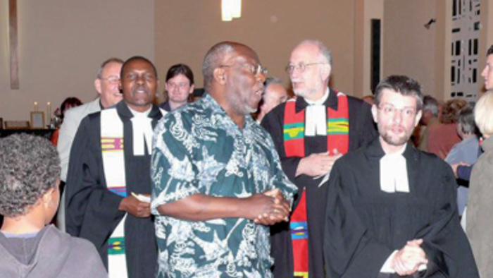 Mehrere Menschen stehen in einer Kirche beieinander; einige tragen Talare oder bunte Stolen und sind im Gespräch mit der Gemeinde.