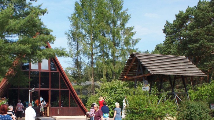 Eine Finnhütte in einem waldigen Gelände. Ein paar Personen stehen rundherum und schauen auf den Eingang.