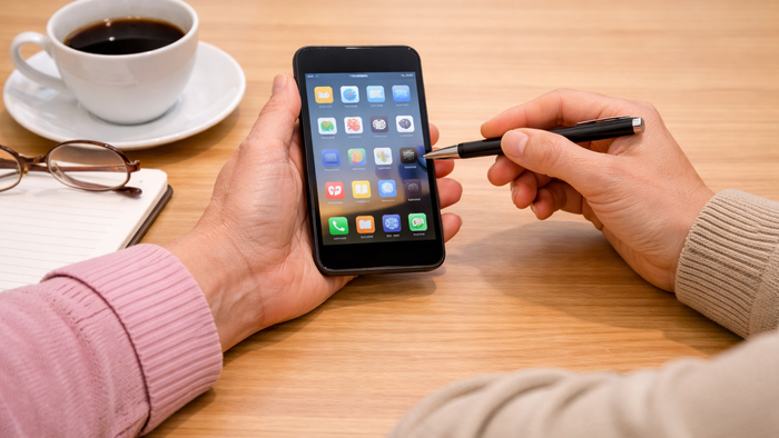 Person, die einen Stylus auf einem Smartphone benutzt, während sie einen Kaffee und ein Notizbuch in der Nähe hält.