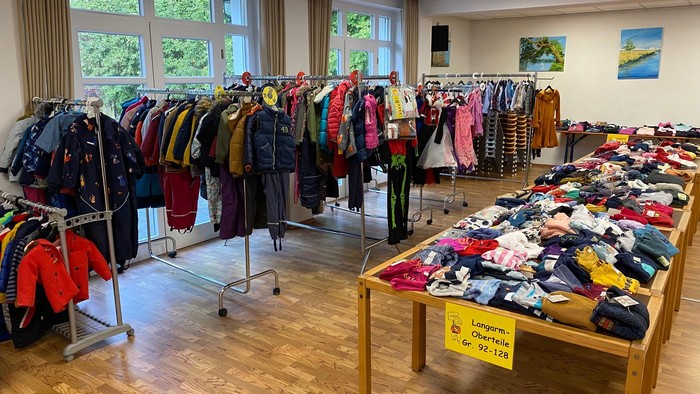 Ein Raum mit Kleidung auf Ständern und Tischen, ein Schild zeigt 