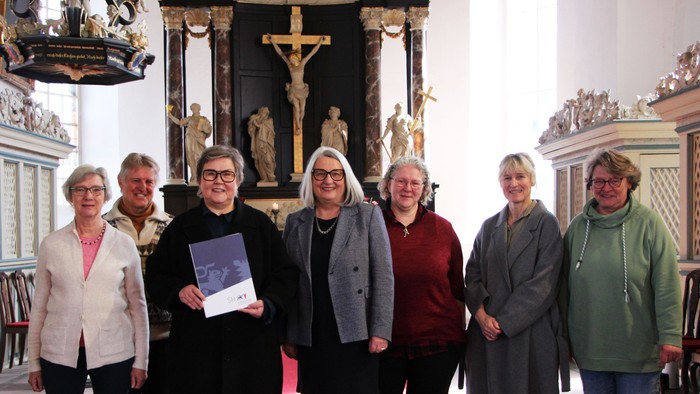 Gruppe von Personen, die drinnen in der Nähe eines kunstvollen Kirchenaltars posieren und ein Buch halten.