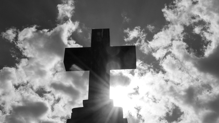 Ein Kreuz vor einem bewölkten Himmel