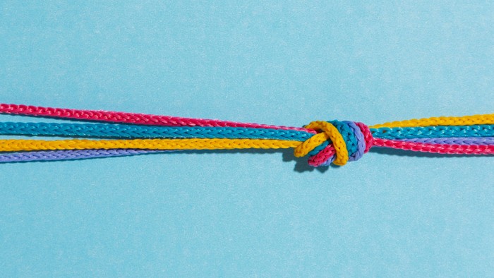 Bunte geflochtene Schnur, zu einem einfachen Knoten gebunden, vor einem hellblauen Hintergrund.