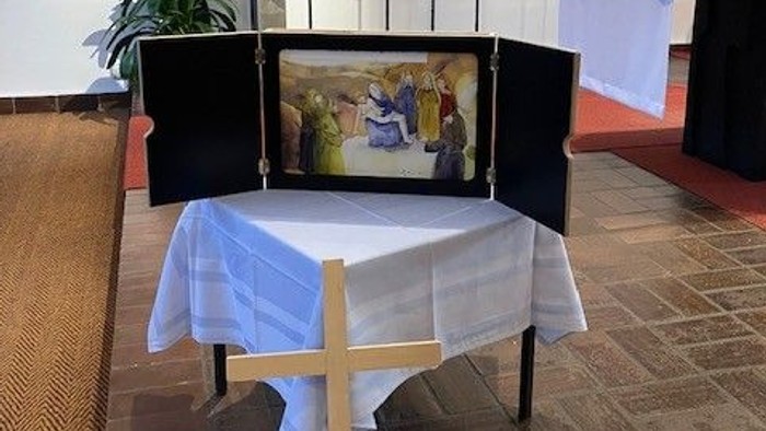 Religiöser Altaraufbau mit Kerzen, Kreuz, gerahmten Kunstwerken und einem drapierten Tisch in einer Kapelle.