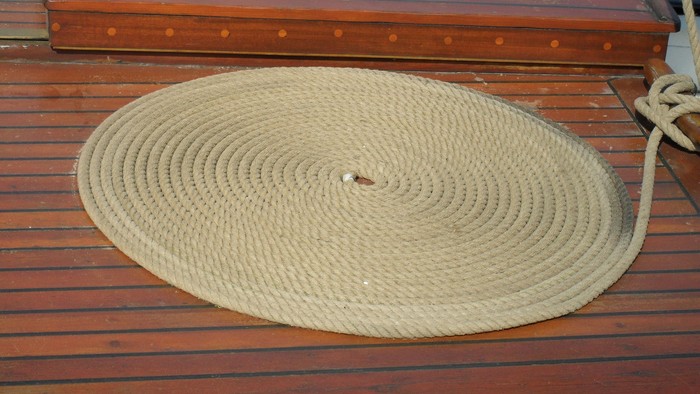 Eine aufgewickelte beige Seilmatte, ausgelegt auf einem Holzdeck in der Nähe des Bootsrandes.