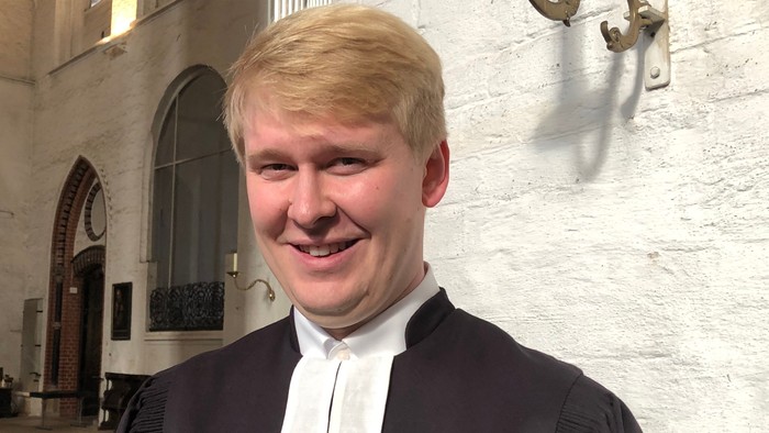 Ein junger Mann in richterlicher Robe vor einem Gebäude