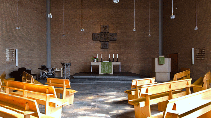 Moderne Kircheninnenausstattung mit Holzbänken, minimalistischem Altar und hängenden Pendelleuchten an strukturierten Wänden.