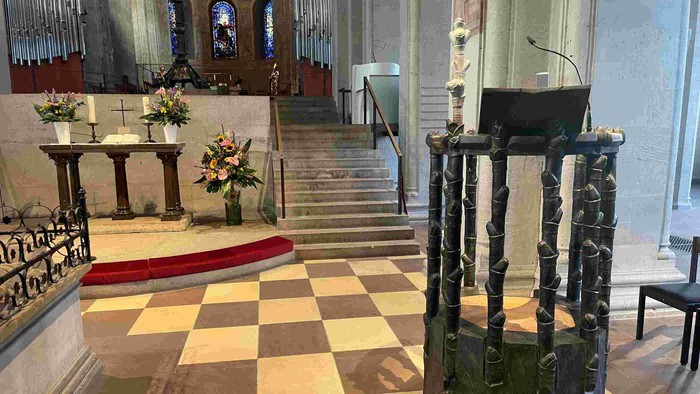 In der Kirche steht ein Pult auf einem Schachbrettboden, umgeben von Blumen und Stufen.