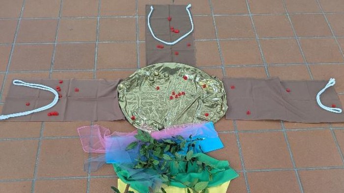 Bunte Stoff- und Folienkunst in menschlicher Form auf dem Gehweg, verziert mit dekorativen roten Punkten.