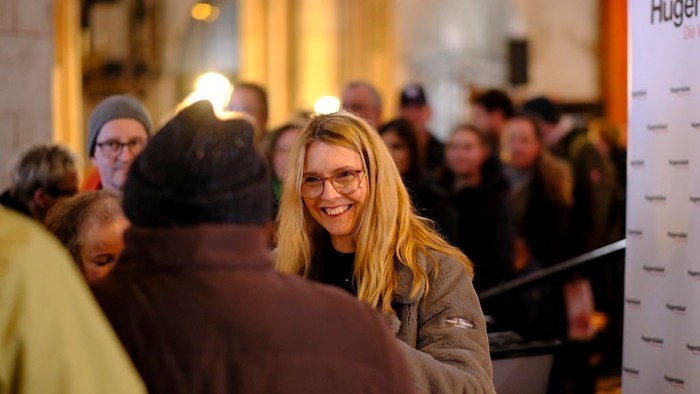 Eine fröhliche Frau lächelt herzlich, während sie auf einer Veranstaltung oder Zusammenkunft von einer Menschenmenge umgeben ist.