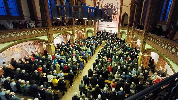 Eine bis auf den letzten Platz gefüllte Kirche, in der das Publikum geschlossen schweigend steht, während Chor und Orchester vorne versammelt sind