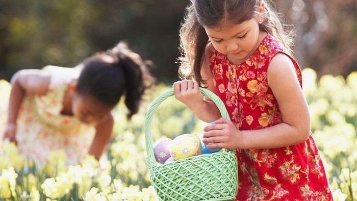 Two young girls in a field of yellow flowers, one holding a basket with Easter eggs.