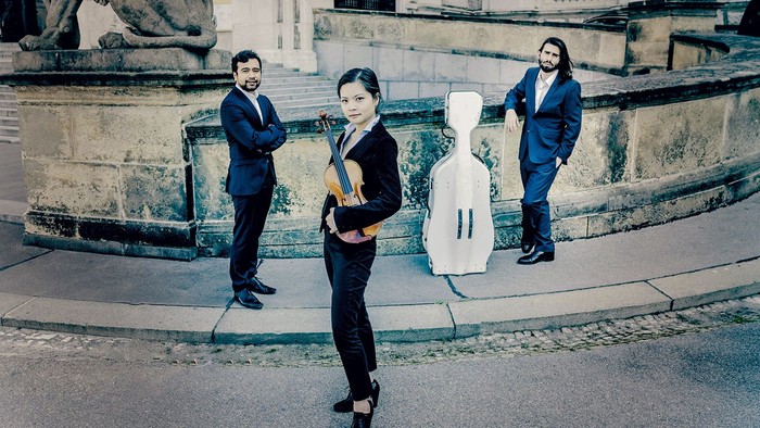 Musikere i formelt tøj poser med en cello på store arkitektoniske trapper.