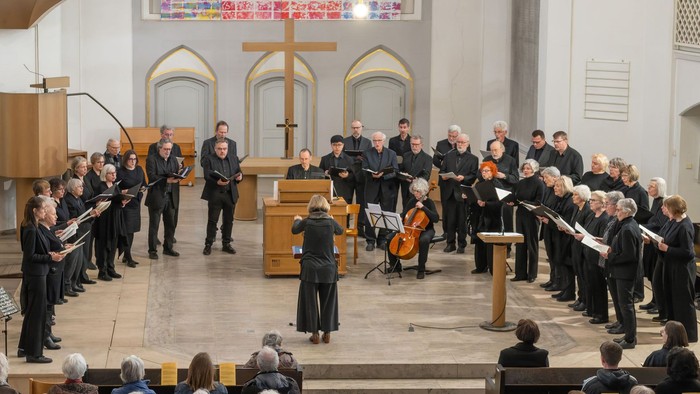 Ein Chor und ein Instrumentalensemble treten in einer Kirche auf, dirigiert von einem Dirigenten vor einem aufmerksamen Publikum.