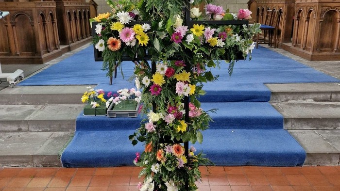Elaborate floral cross arrangement placed on a church altar with blue carpeted steps.