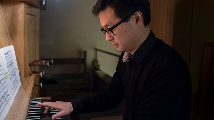 Yngre mand med mørke briller spillende på kirkeorgel. 