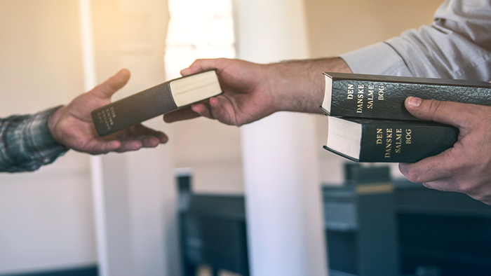 To personer udveksler religiøse bøger i en kirke med synligt "Folkekirken"-branding.