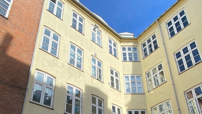 Udsigt til en gårdsplads i en etageejendom med store vinduer og byggematerialer spredt rundt omkring.