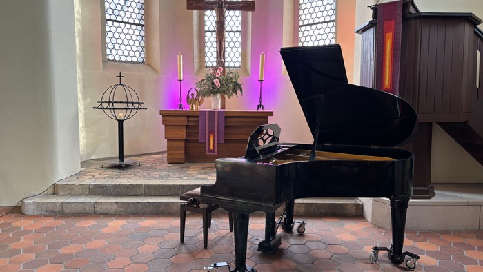 Ein Flügel steht in einem ruhigen Kirchenschiff nahe einem Altar mit Kerzen und einem Kreuz.