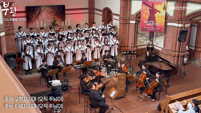 Ein Kirchenchor mit Orchester führt ein musikalisches Stück in einer festlich geschmückten Kirche auf.
