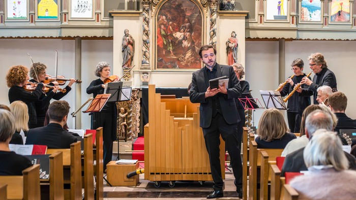 Ein Mann singt vor einem kleinen Orchester in einer Kirche