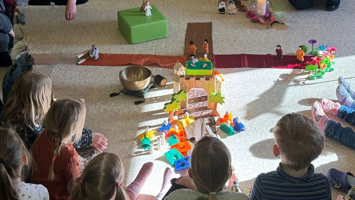 Kinder versammeln sich um eine Erzählstunde mit musikalischer Begleitung und einem farbenfrohen Diorama-Aufbau.