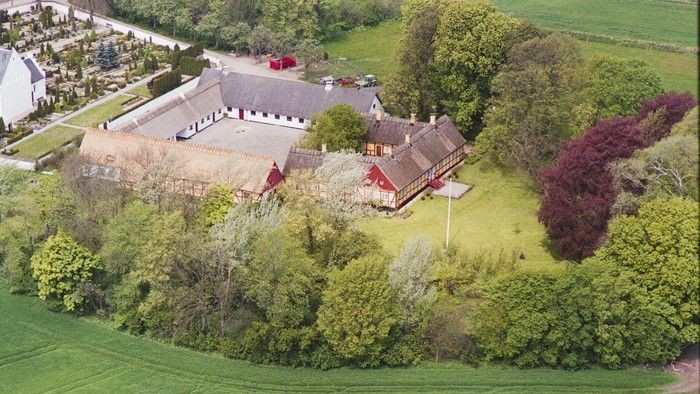 En stor gård med røde tag og omgivelser af grønne skove og enkehage.