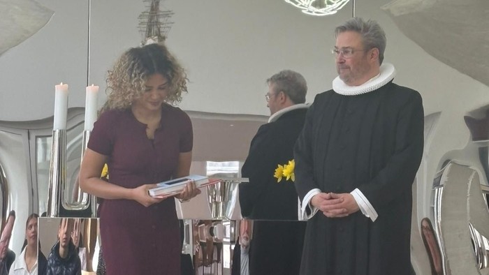 To personer, den ene iført gejstligt tøj og den anden i formelt antræk, deltager i en ceremoniel begivenhed.