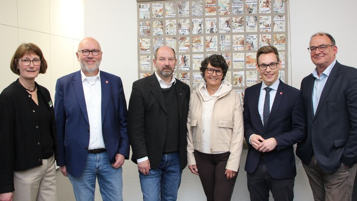 Gruppe von fünf Personen, die in einer Galerie vor einer farbenfrohen Mosaikkunst-Ausstellung posieren.