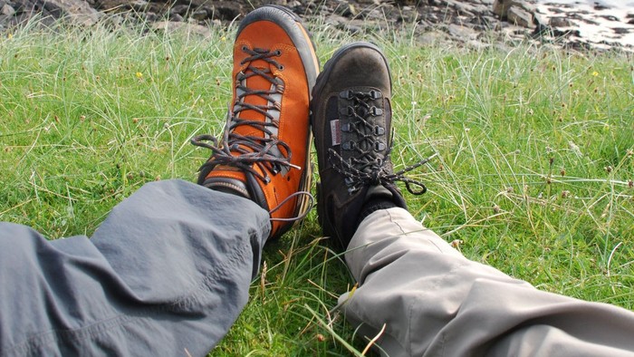 Beine mit Wanderschuhen auf einer grünen Wiese mit Felsen am Meer