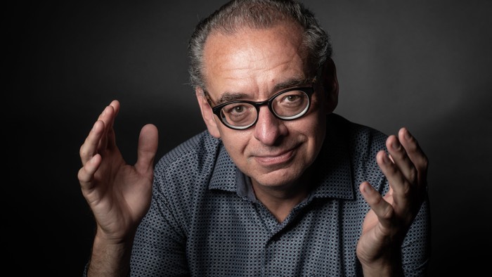 En mand med briller og graue hår, der skaber en dramatisk effekt med sine hænder.