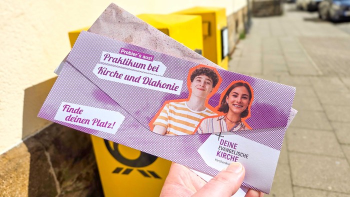 Zwei Briefe der Kirchenpost werden vor Briefkästen gehalten