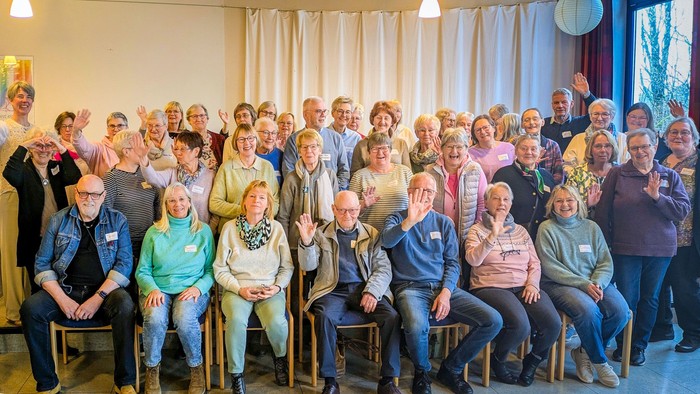Viele Menschen in einem Saal winken in die Kamera