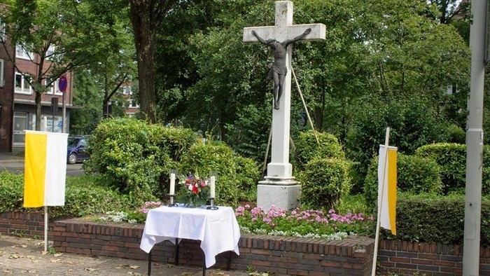 Ein Kreuz steht in einem Garten mit weißen Tisch und gelben Fahnen.