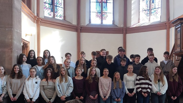 Gruppe junger Leute, die gemeinsam in einer Kirche mit bunten Glasfenstern und einer Orgel posieren.